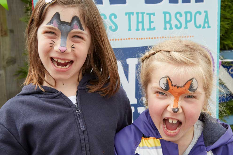 Two girls wearing animal themed face paint smiling.