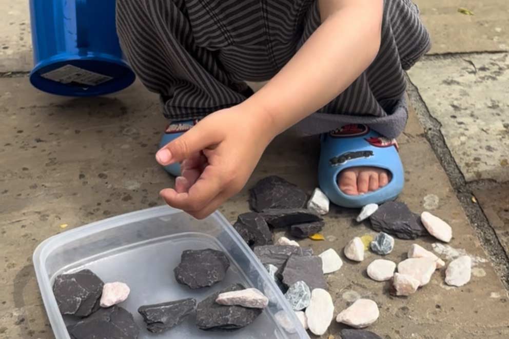 Jude placing small rocks and stones into a plastic container.